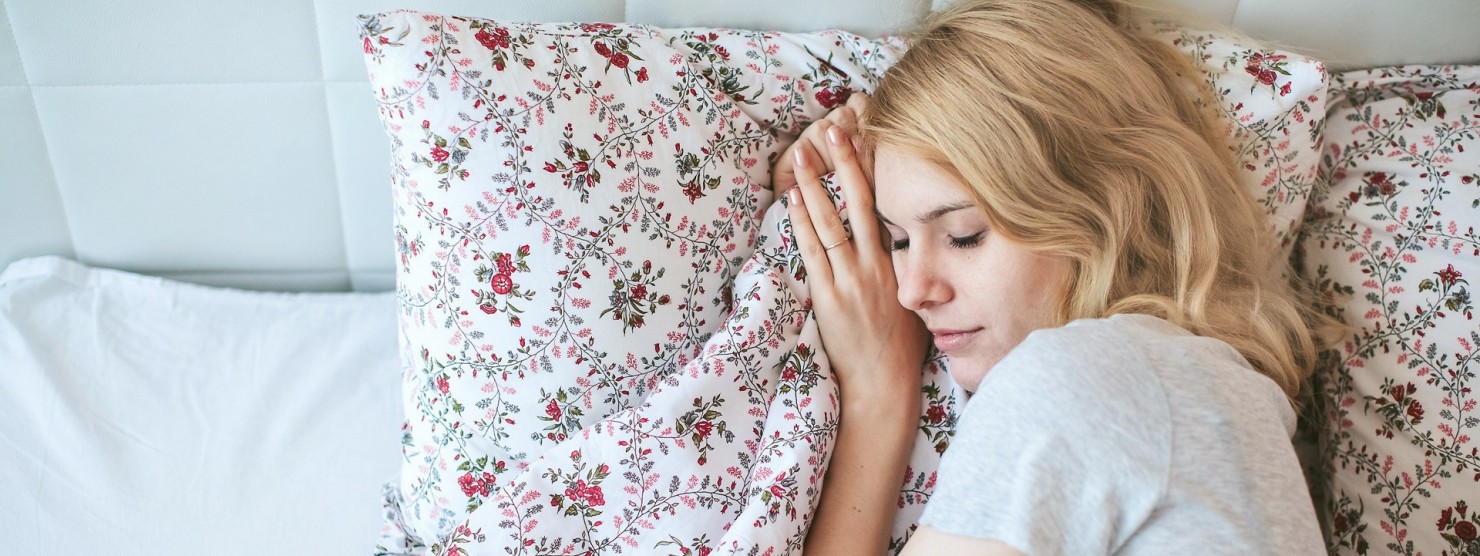 Eine blonde Frau liegt in einem weißen Bett und schläft.