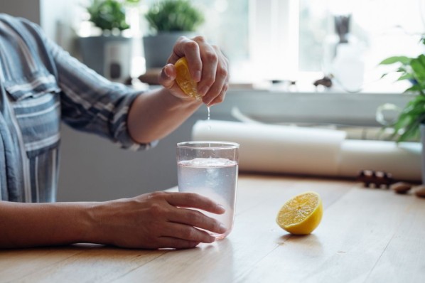 Mann mit Wasserglas, der eine Zitrone ausdrückt.