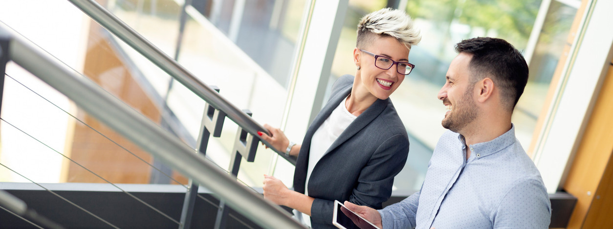 Zwei Kollegen bewegen sich in ihrem Arbeitsalltag und laufen die Treppe hoch.