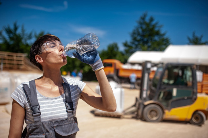 Eine Bauarbeiterin trinkt Wasser aus einer Flasche.