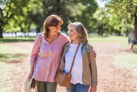 Zwei Seniorinnen spazieren gemeinsam durch einen schönen Park. 