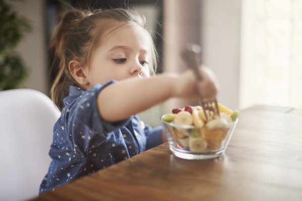 Ein etwa 3-jähriges Mädchen isst Obstsalat aus einer kleinen Glasschüssel