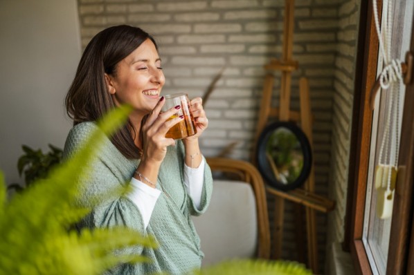 Eine Frau Mitte 40 steht mit einer tasse Tee am fenster