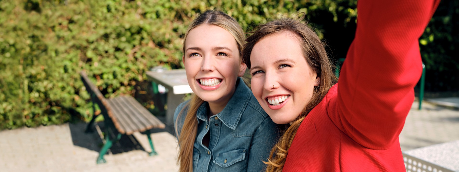 Die Auszubildenden Alina und Josi sitzen in einem Park auf einer Tischtennisplatt und machen gemeinsam ein Selfie.