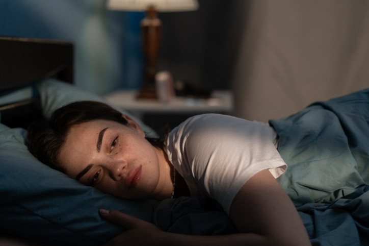 Eine etwa 25-jähriger Frau liegt nachts im Bett wach. Licht von draußen scheint in das Schlafzimmer und in ihr Gesicht.