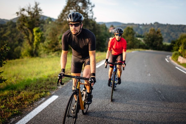 Ein etwa 40-jähriges Paar fährt Rennrad auf einer Straße.