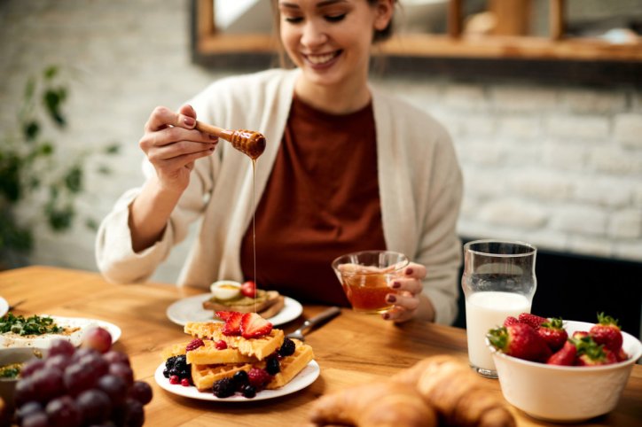 Eine Frau verfeinert ihre Pancakes mit Honig