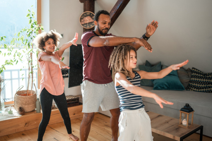 Eine Familie tanzt gemeinsam zuhause im Wohnzimmer.