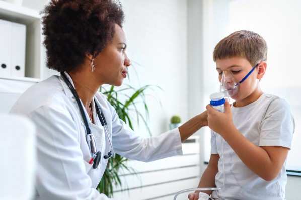 Eine Ärztin versorgt einen etwa 7 jährigen Jungen mit einem Inhalator.