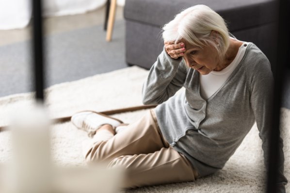 gestürzte Seniorin auf Teppich sitzend berührt Stirn mit der Hand