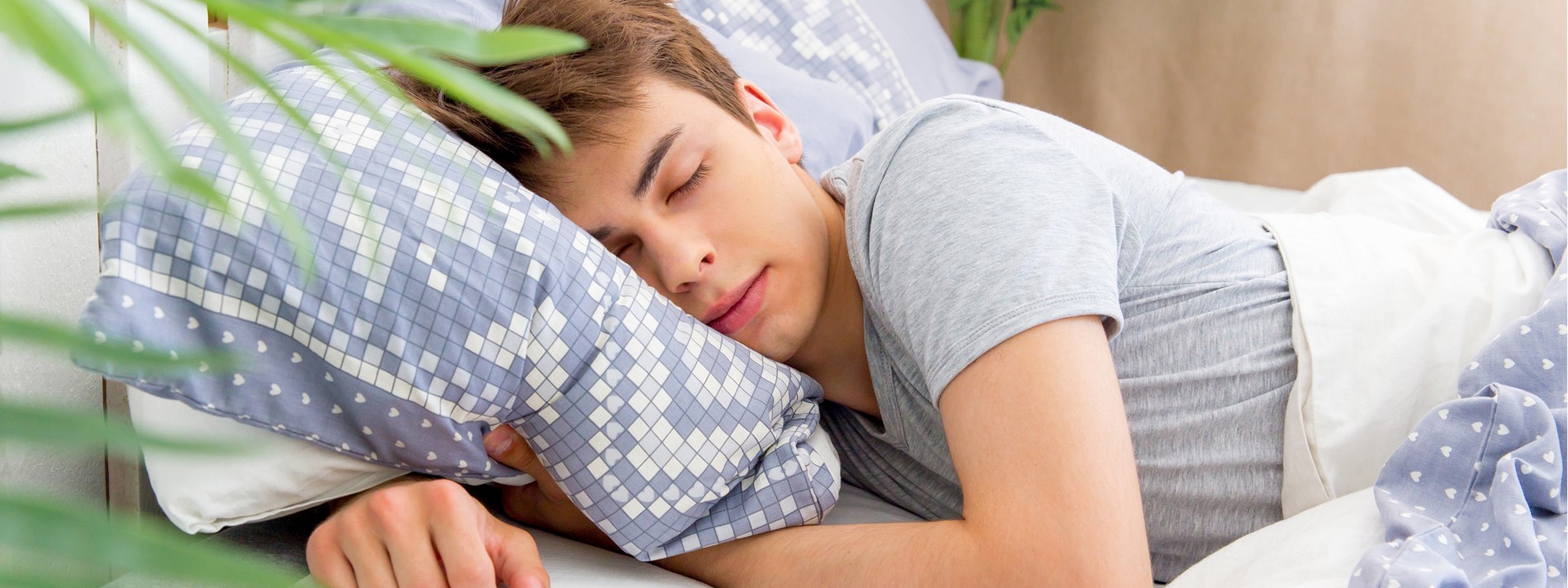 Junger Mann Anfang 20 liegt gemütlich im Bett und schläft.
