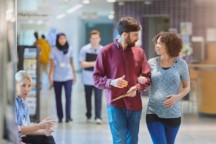 a mid adult couple walk through a hospital corridor heading for an early stage pregnancy check