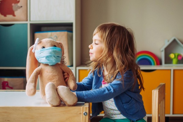 Caö 4-jähriges Mädchen sitzt neben ihrem Stoffhasen. der Hase trägt eine OP-Maske