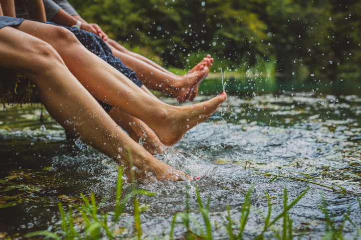 Personen planschen mit den Füßen im Wasser eines Sees.