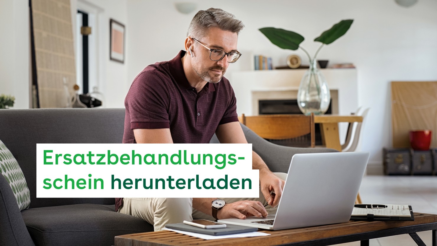 Ein Mann, Mitte 40, sitzt zuhause auf dem Sofa. Er arbeitet an einem Laptop, der vor ihm auf dem Couchtisch steht. Auf dem Couchtisch liegen ein Kalender und ein Smartphone. Er trägt einen kabellosen Kopfhörer.