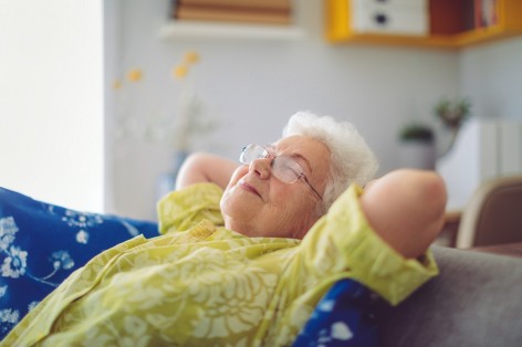 Seniorin mit Bille und grauen Locken entspannt sich zu hause auf dem Sofa.