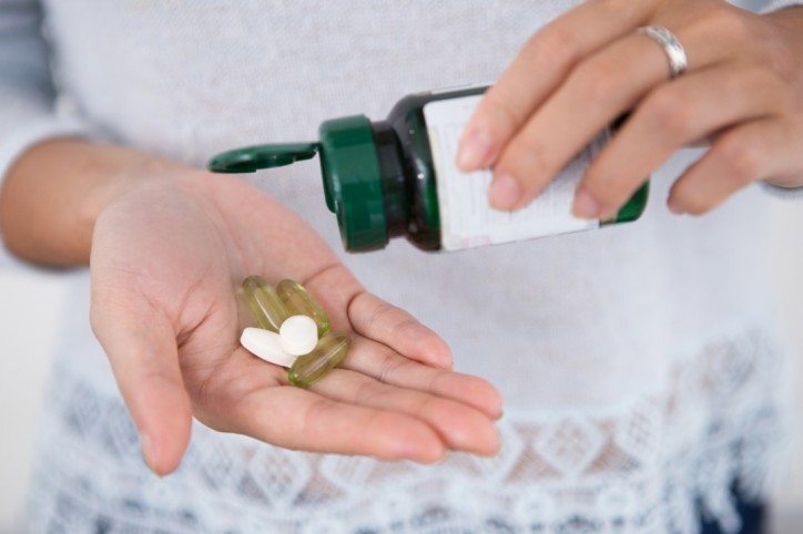 Cropped view of woman pouring pills from bottle onto palm. Front view.