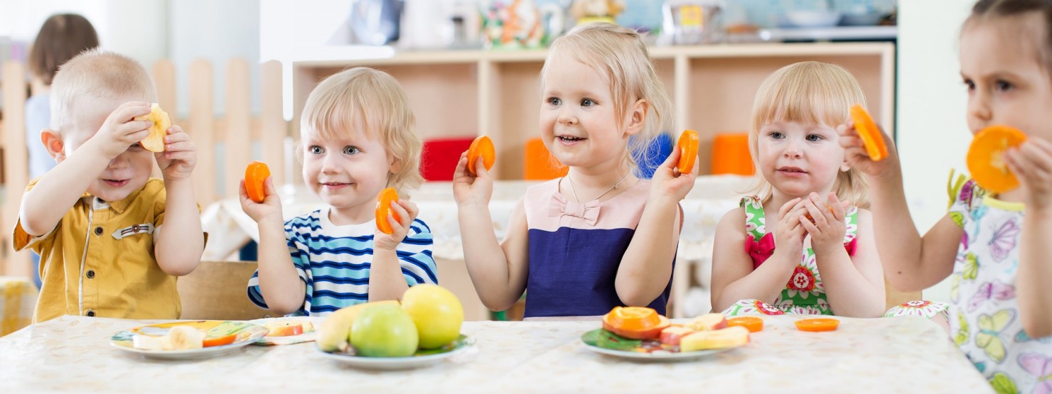 Kinder an einem Esstisch in einer Kita beim Essen.