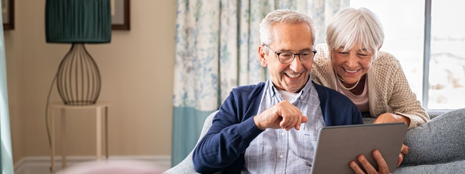 Ein Seniorenpaar schaut gemeinsam lächeln auf ein Tablet.