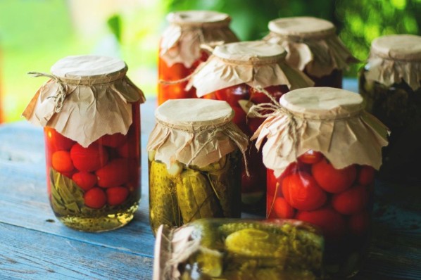 Auf einem Holztisch im Garten stehen verschiedene fermentierte Gemüsesorten in Gläsern.