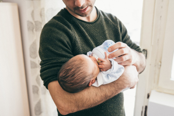 Ein Vater hält sein neugeborenes Baby auf dem Arm und füttert es mit dem Fläschchen.