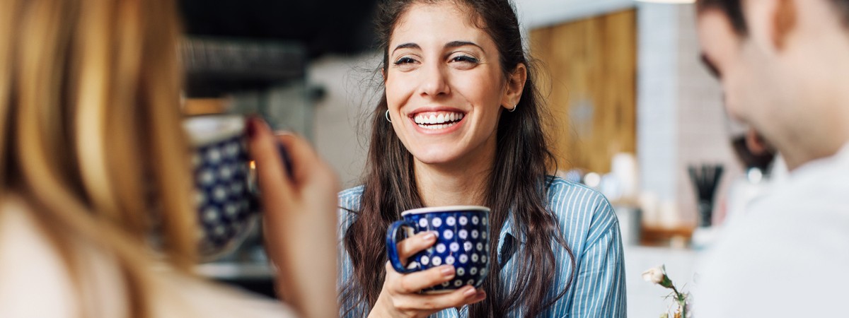 Eine 35-jährige Frau unterhält sich gut gelaunt bei einem Kaffee mit ihren Freunden.