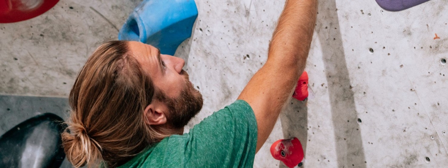 Ein junger Mann klettert in einer Boulder-Halle. 