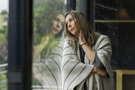 eine Frau steht nachdenklich am fenster und lehnt ihren Kopf gegen die Fensterscheibe