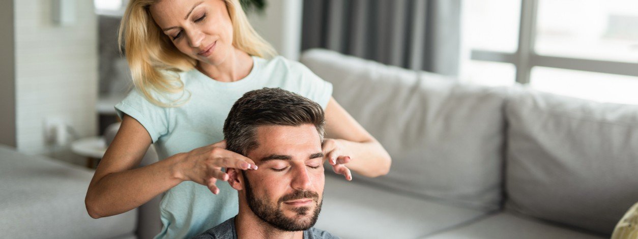 Ein Mann erhält von seiner Partnerin eine Akupressurmassage am Kopf.