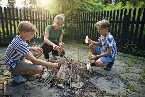 Drei Kinder spielen im Garten und bauen ein Lagerfeuer.