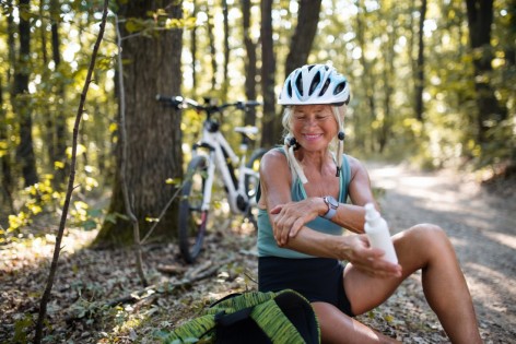 Ältere sportliche Frau legt eine Pause beim Radfahren ein, um Sonnenschutz mittel aufzutragen.