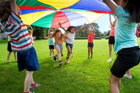 Kindergruppe spielt mit einem bunten Fallschirmtuch.