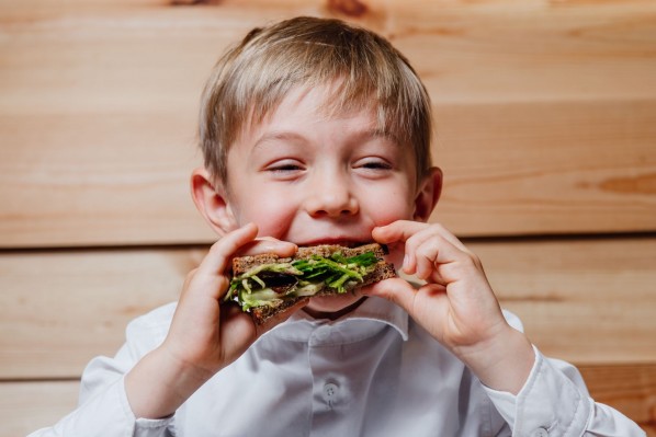 Ein etwa 5 jähriger Junge isst eine zusammen geklappte Schnitte mit Grünzeug. Dabei lächelt er und genießt.