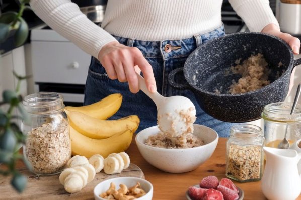 Frau, die Haferflocken in eine Schüssel gibt und Porridge zubereitet.