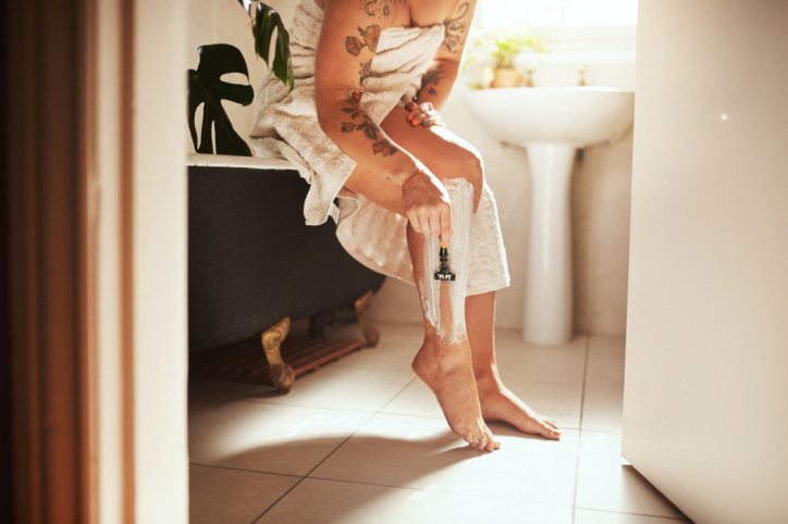 Eine etwa 25 jährige Frau liegt in einer Badewanne und rasiert sich die Beine.