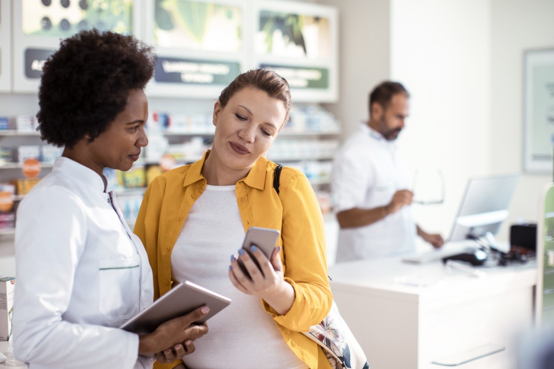 Apothekerin, der einer schwangeren Frau bei der Auswahl des richtigen Produkts in einer Apotheke hilft