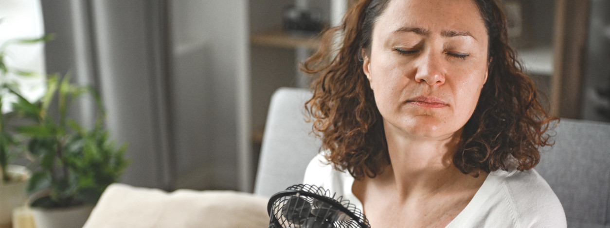 Eine Frau versucht Hitzepickel zu verhindern indem sie sich mit einem Ventilator abkühlt.