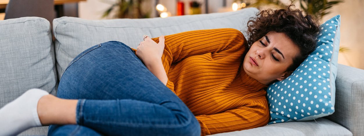 Eine Frau mit Schmerzen durch Adenomyose liegt auf dem Sofa