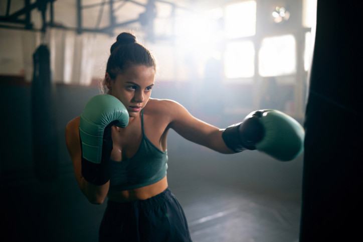 Eine junge Frau holt beim Boxen zum Schlag auf einen Boxsack aus