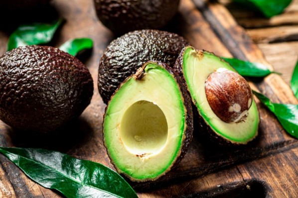 Eine aufgeschnittene Avocado und weitere Avocados auf einem Tisch.