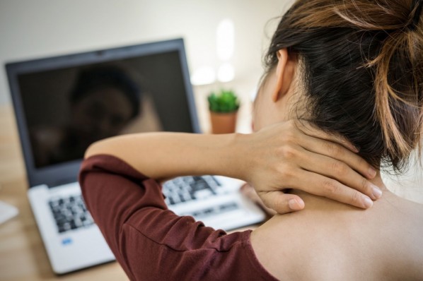 Junge Frau mit Nackenschmerzen sitzt vorm Laptop. 