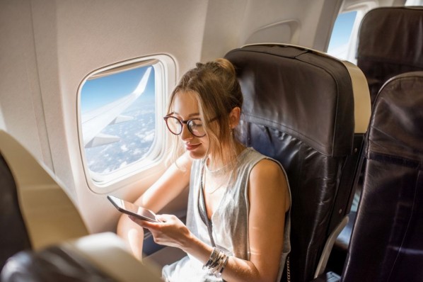 Eine etwa 25 jährige Frau sitzt in einem Flugzeug und schaut auf ihr Handy.