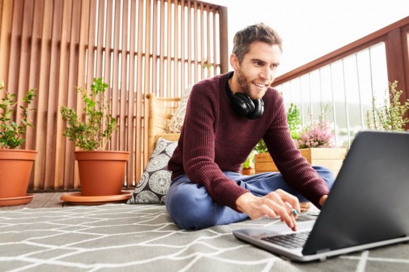 Happy young man sitting in balcony and working on laptop