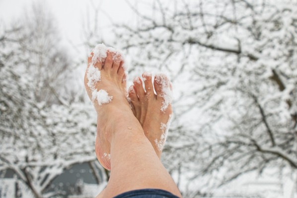 Schnee bedeckte Füße einer Frau vor einer tief verschneiten Winterlandschaft.