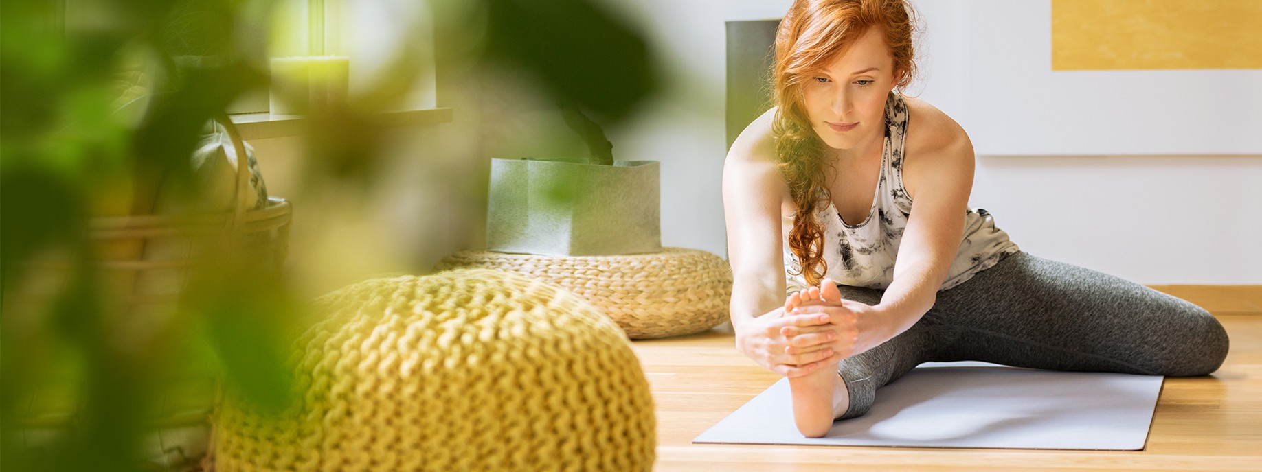 Eine circa 30-jährige Frau mit roten Haaren macht zu Hause Dehnübungen auf einer Yogamatte.