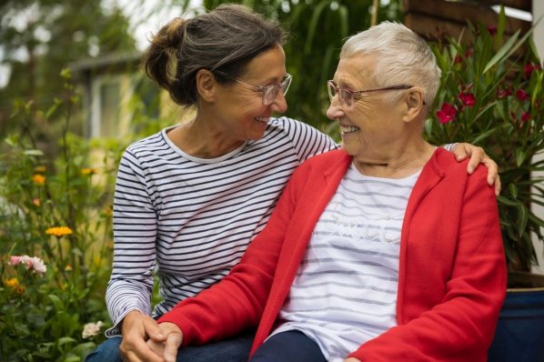 Eine Seniorin sitzt mit ihrer Tochter im Garten.