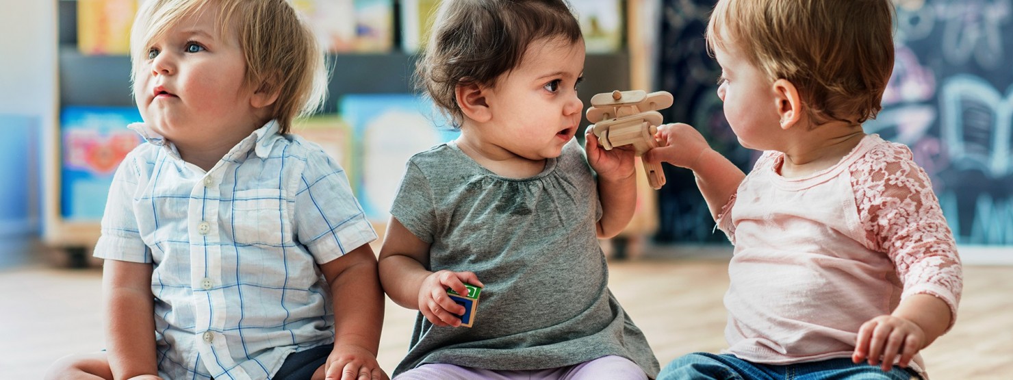 Drei Babys sitzen zusammen und spielen mit bunten Bausteinen.