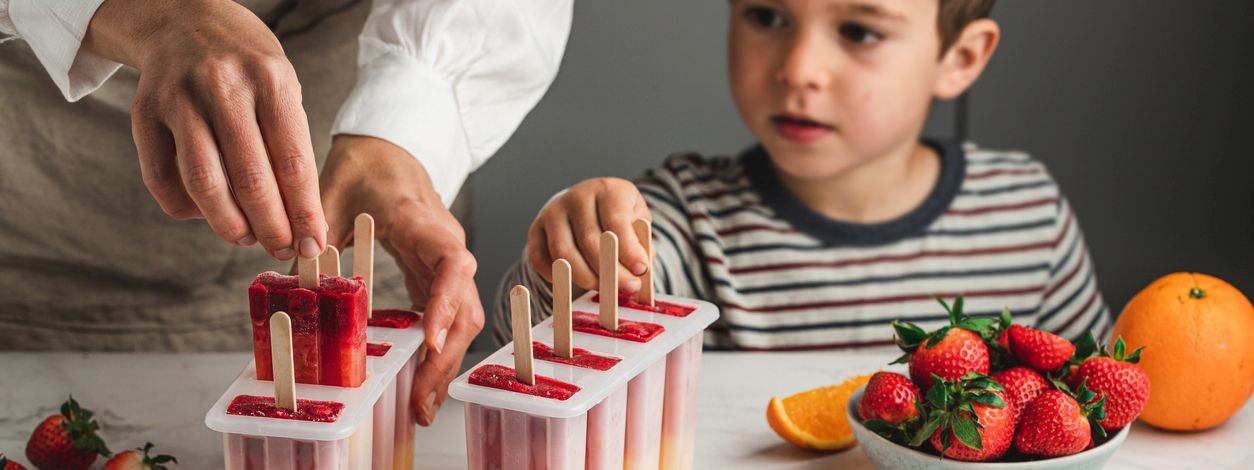 Ein etwa 4 jähriger Junge hilft seiner Mutter bei der Herstellung von gesundem Wassereis. 