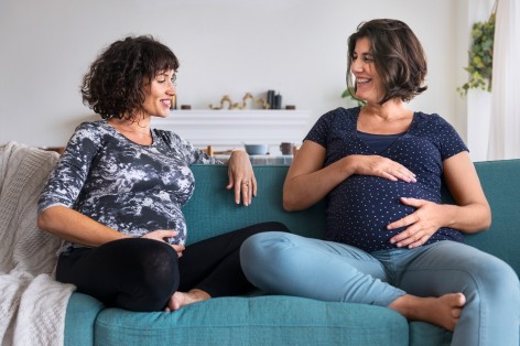Zwei schwangere Frauen auf einem Sofa unterhakten sich.