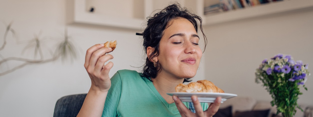 Junge Frau mit schwarzen locken lässt sich ein Croissant schmecken